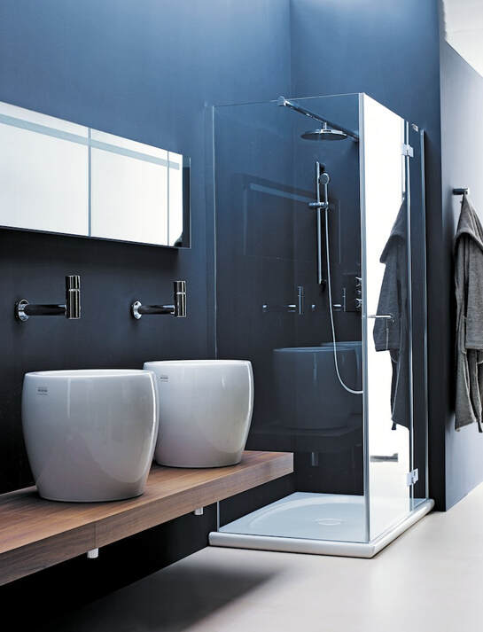 Blue modern bathroom with Laufen white fireclay vessel sinks on a walnut counter and chrome wall mount faucets next to a custom glass shower