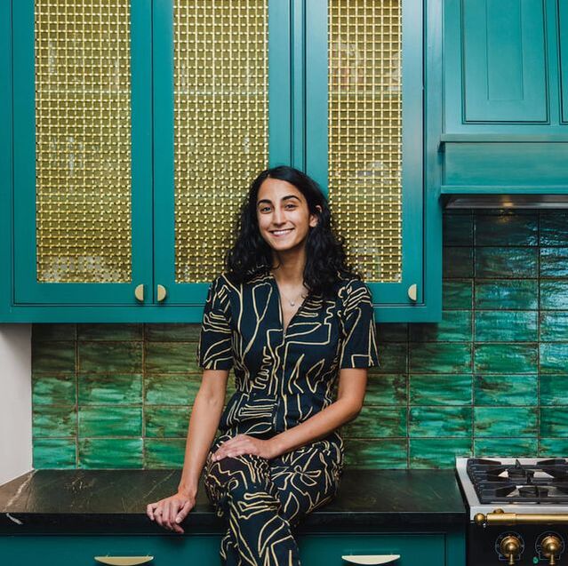 Priya founder of hapny hardware in front of green cabinets and brushed brass half moon pulls