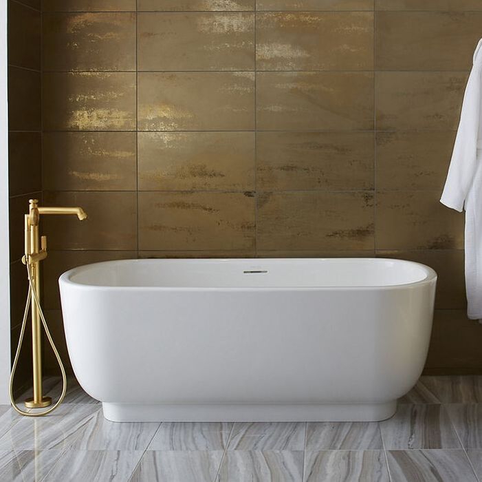 Luxurious gold bathroom with a kallista freestanding bath and unlacquered brass tub filler in front of gold tile wall