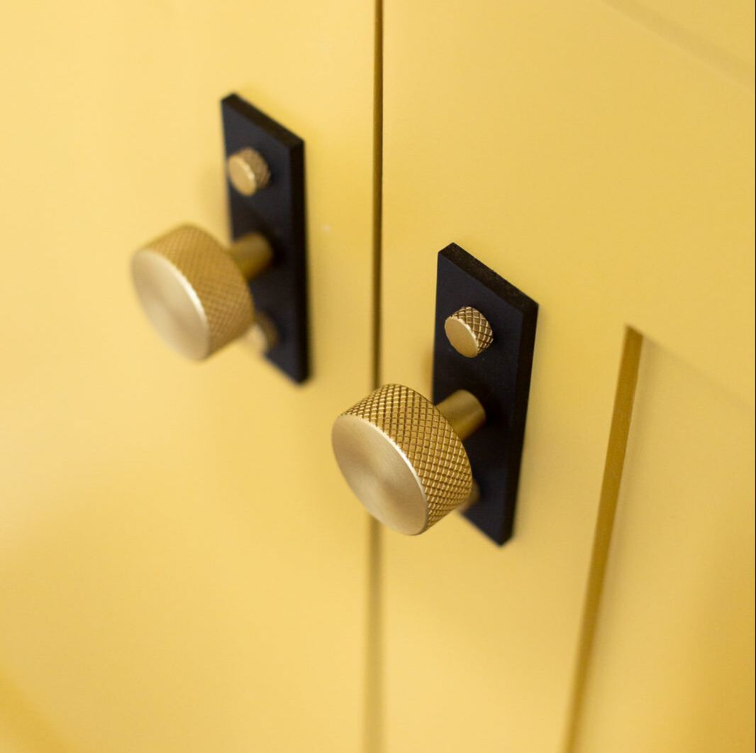 Armac Martin Mix series black and gold cabinet hardware with knurled knobs in a two tone finish on a yellow cabinet