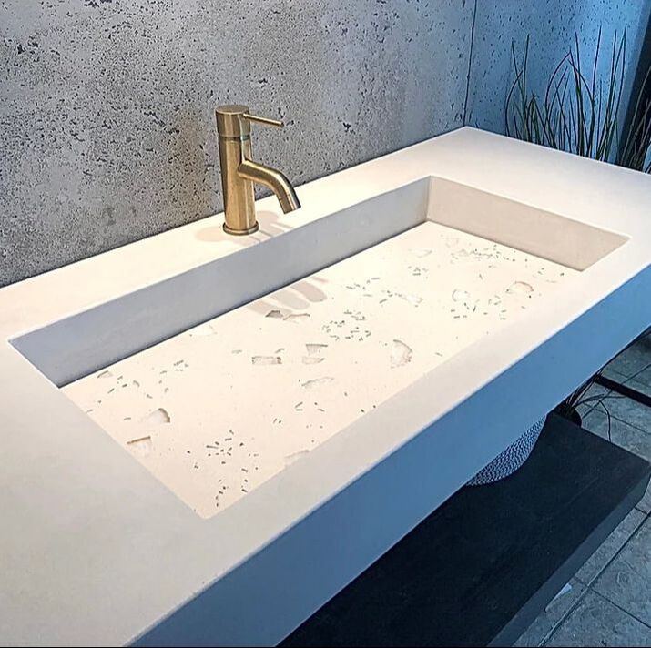 Balux concrete wall mount sink with an undermount terrazzo lavatory, a gold faucet and concrete wall complete the bathroom