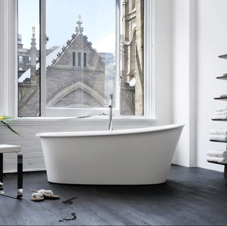 Canadian freestanding bathtub by wetstyle in a loft apartment bathroom and chrome tub filler and large window