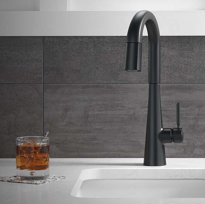 Delta Monrovia matte black kitchen faucetandle and undermount sink on a marble counter with a glass of whisky on ice