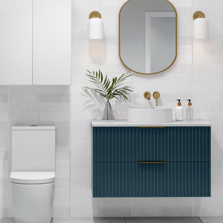 Wall hung vanity with blue fluted drawers in a modern bathroom with a round vessel sink and gold accents and a modern dual flush toilet
