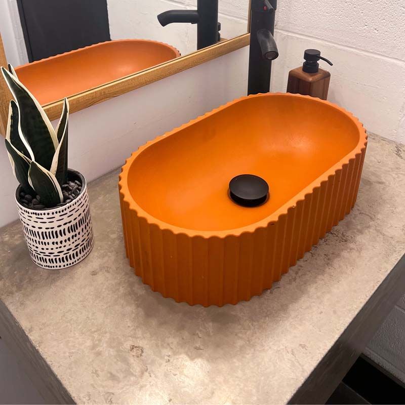 Orange concrete bathroom sink made in canada on quartz countertop with matte black faucet and gold mirror