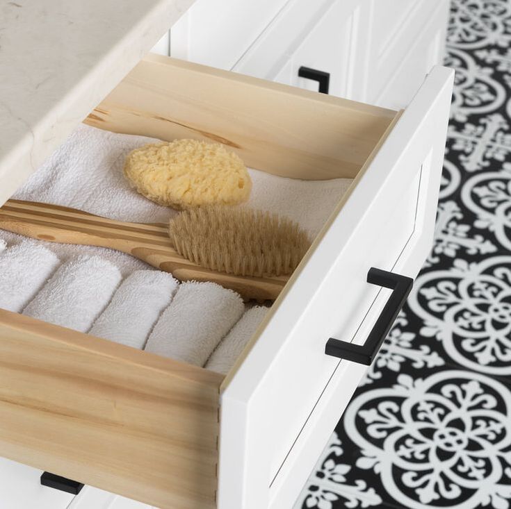 Drawer interior of Stonewood classic white vanity with bath accessories inside above a black and white cement tile floor