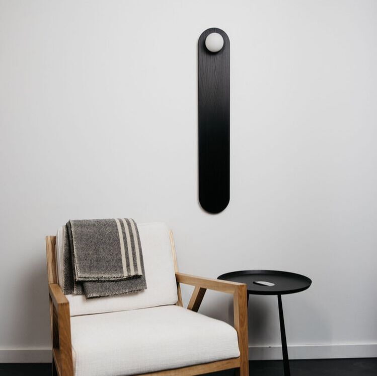 tomnuk tablet 36 black ash wall sconce on the wall above a midcentury modern white and wood chair with a grey throw and simple black side table