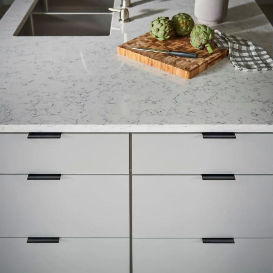 Topknobs matte black edge pull on light grey drawers in a modern kitchen with quartz countertop
