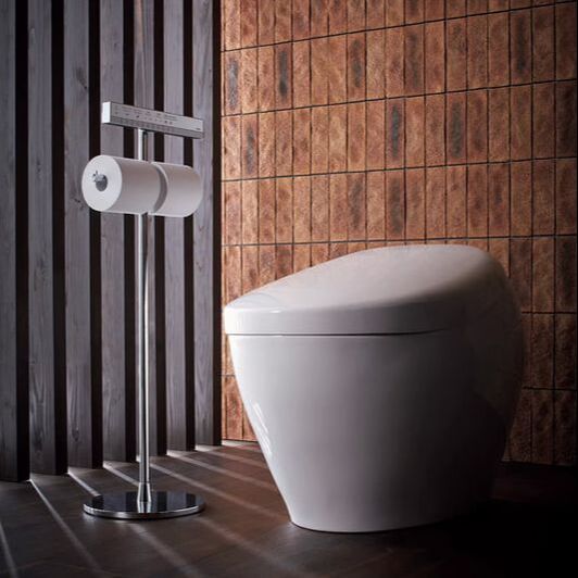 White Toto Neorest washlet bidet toilet in front of a brown tile wall and black slat wall next to a chrome freestanding toilet paper holder