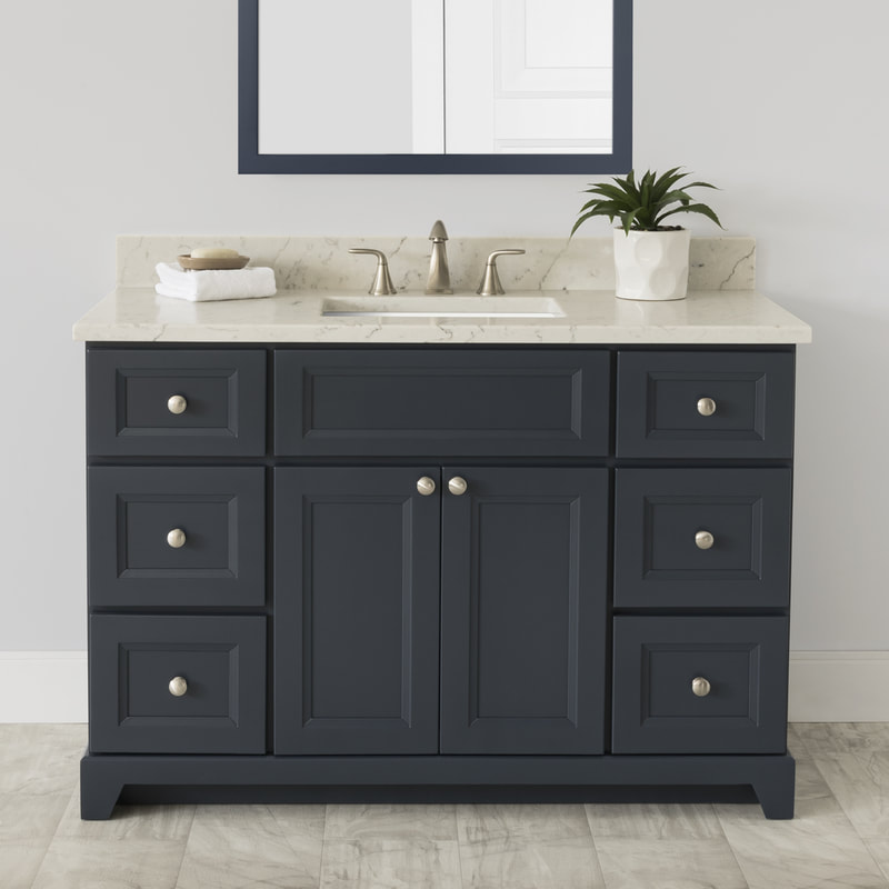 Stonewood four foot wide vanity with a quartz countertop and matching wood framed mirror. on the counter is a small plant in a white pot next to a brushed nickel widespread faucet